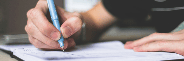 Close-up of a person writing on a sheet of paper with a blue pen.