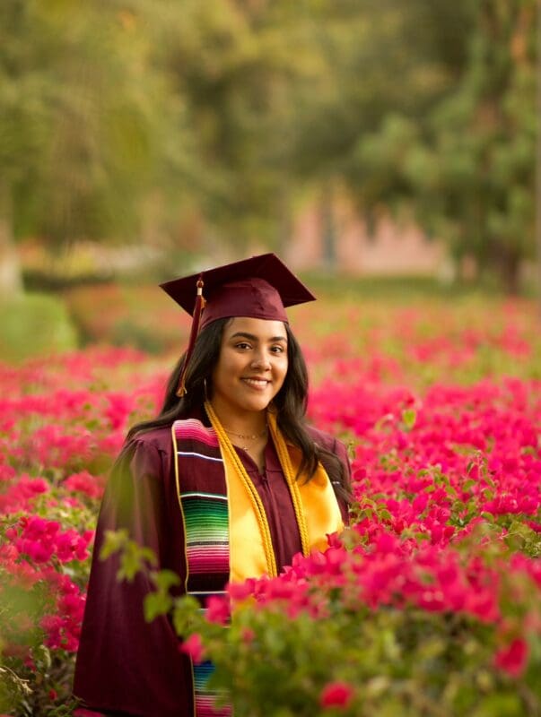 Graduate in cap and gown posing among colorful flowers outdoors
