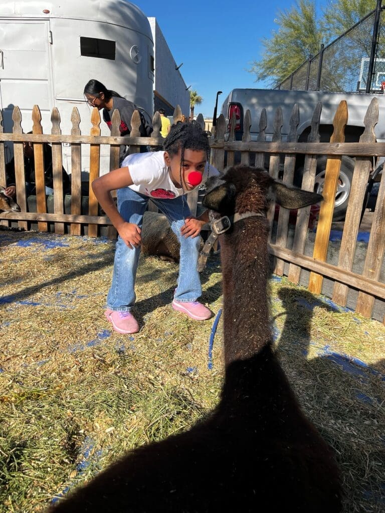 Student interacting with a goat during an outdoor animal activity at a New Pathways for Youth event