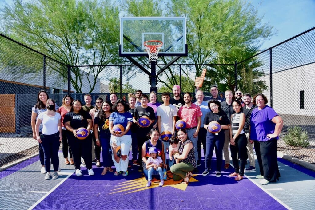 New Pathways for Youth participants and mentors celebrate together on a community basketball court during a youth engagement event.