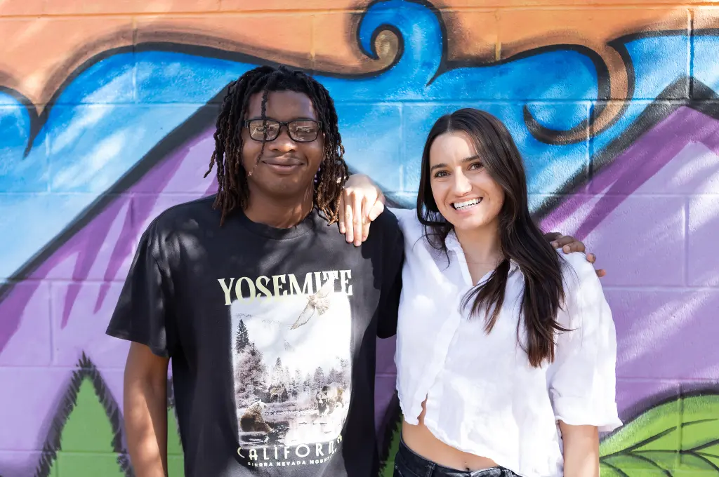 New Pathways for Youth | Tax-Smart Gifts Two young people smiling and posing together against a blue and colorful background.